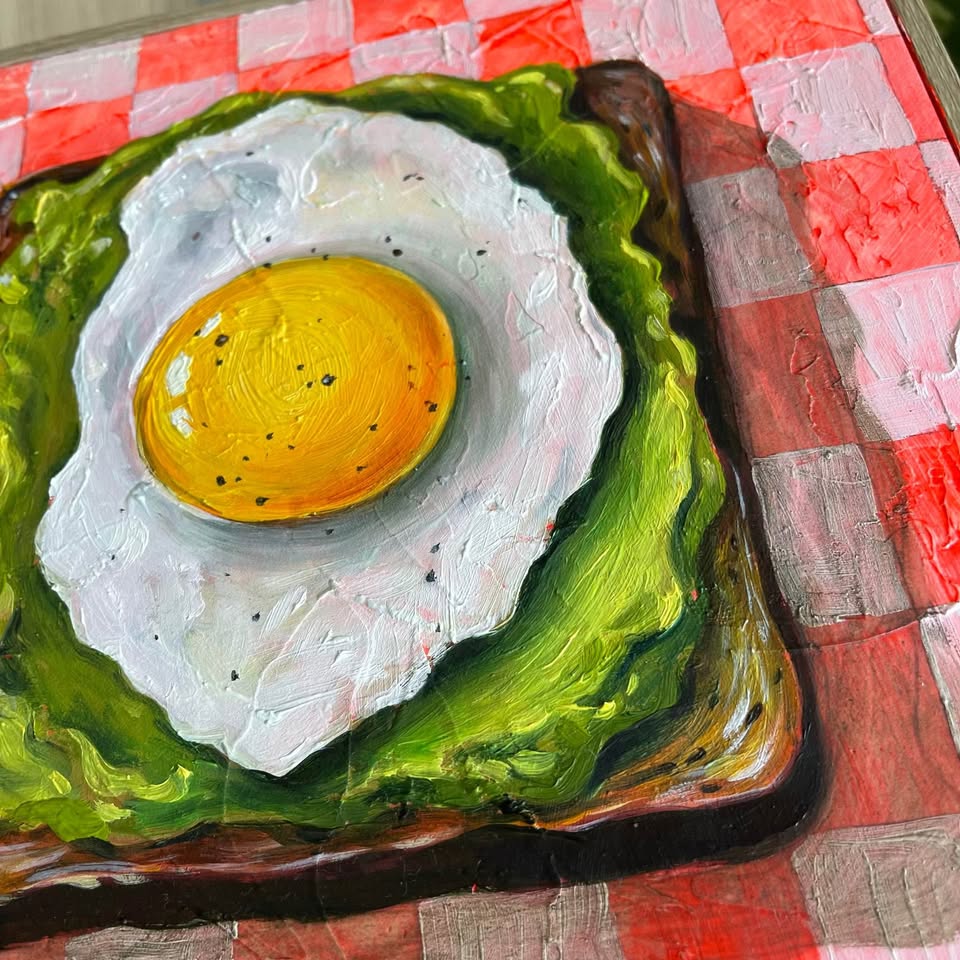 A close-up of a painted food scene showing a fried egg on a slice of toast, placed on a red-and-white checkered tablecloth. The artwork fills most of the frame.