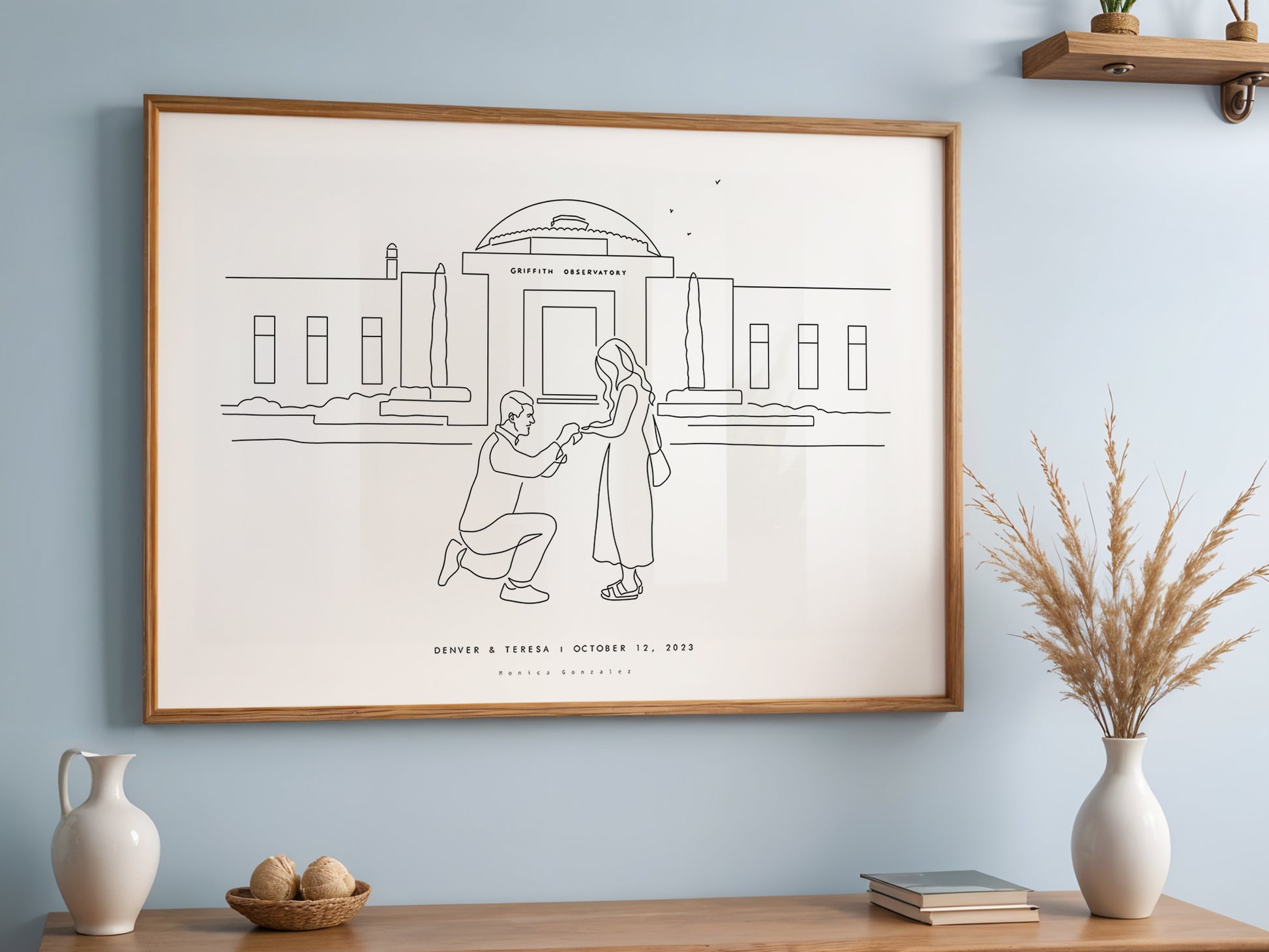 Framed artwork of two people in a line drawing style on a wall with decorative items on the credenza below.