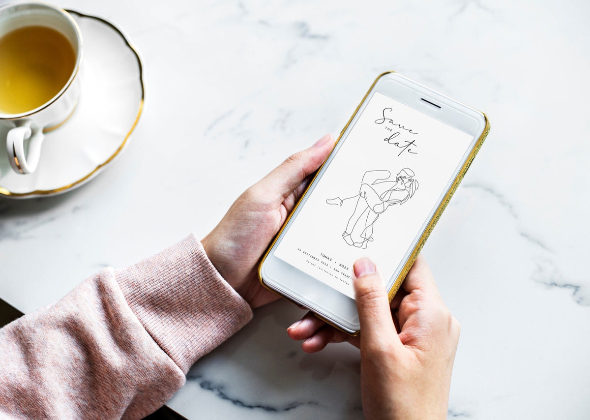 Hands holding a phone with a Save the Date electronic invitation on the screen featuring a line art portrait of a couple kissing
