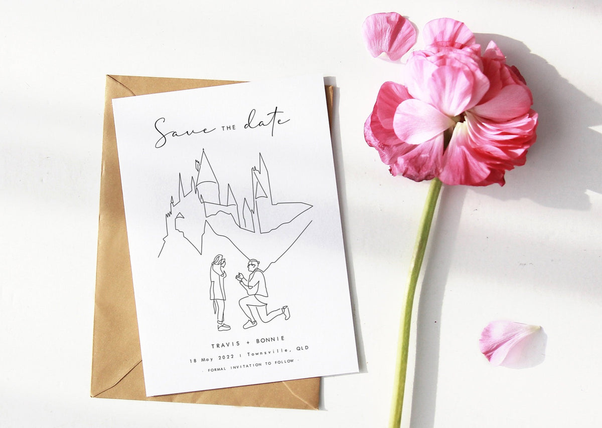 Custom save the date invitation printed on a card with an envelope in the background and a flower next to it. There is a line art portrait of a man proposing to his partner with a castle in the background